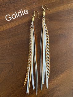 two pairs of feather earrings on top of a wooden table with the words goldie written above them