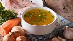 a bowl of soup next to some vegetables and meat