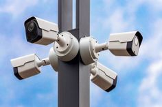 two security cameras mounted on the side of a pole with blue sky in the background