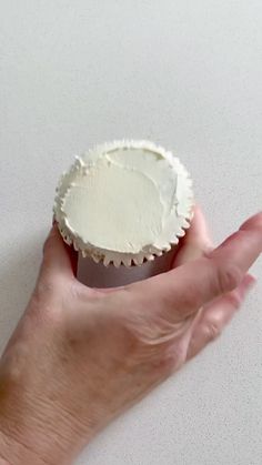 a hand holding a cupcake with white frosting