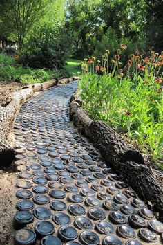 a stone path made out of bottles in the middle of a garden with flowers and trees