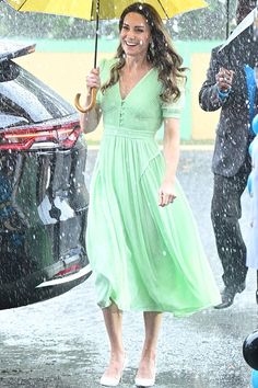 a woman in a green dress holding an umbrella while walking through the rain on a rainy day