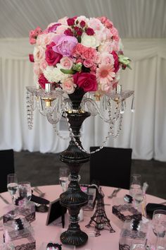 a table topped with a vase filled with pink and white flowers next to wine glasses