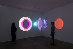 two people standing in front of three brightly colored circles on a white wall with one person looking at it