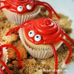 three cupcakes with googly eyes and red icing on them sitting in sand