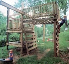 a child on a swing set in the grass near a wooden structure with stairs and ladders