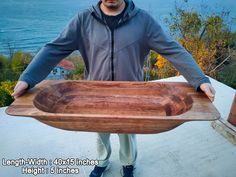 a man holding a large wooden bowl on top of a roof next to the ocean