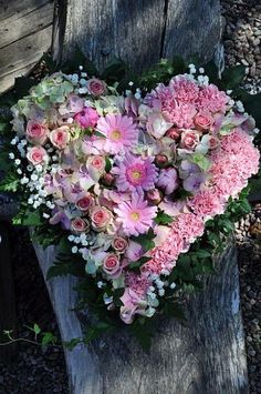 a heart - shaped arrangement of pink and white flowers sits on a piece of wood