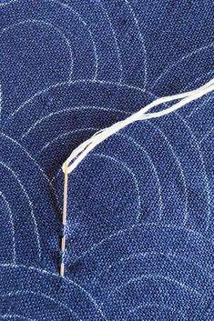 a piece of blue fabric with white thread on it and an orange needle in the middle