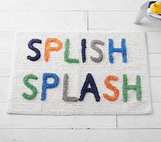 a bath mat with the words splash and an orange rubber duck on it next to a bowl of yellow rubber ducks