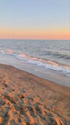 a surfboard sitting on top of a sandy beach next to the ocean at sunset