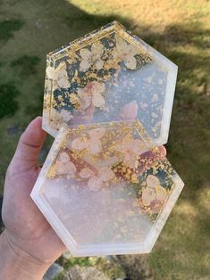 a person holding up two clear boxes with gold flakes on them in the grass