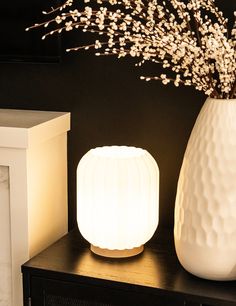 a white vase sitting on top of a wooden table next to a lit up lamp