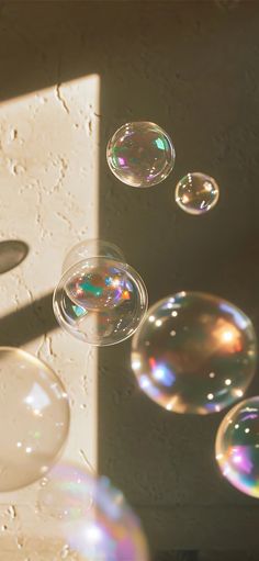 soap bubbles floating in the air next to a white wall with sunlight coming through it