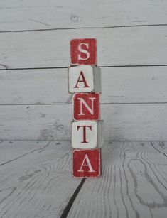 wooden blocks spelling santa on top of a white wood floor with the word santa spelled in red