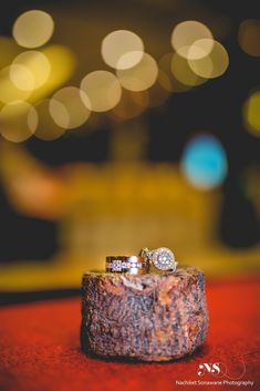 two wedding rings sitting on top of a wooden block in front of some blurry lights