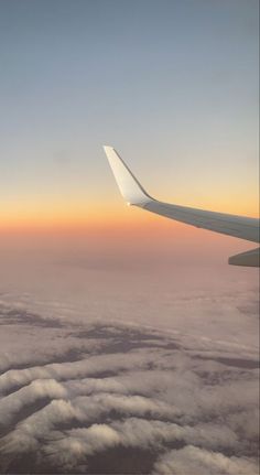 the wing of an airplane as it flies through the sky with clouds and sunset in the background