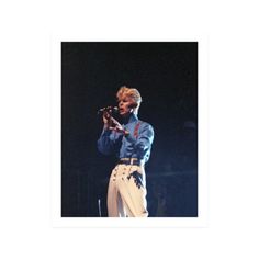 a man in white pants and a blue shirt holding a microphone while standing on stage