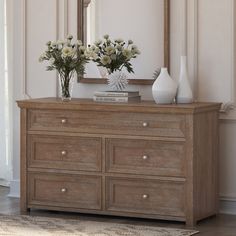 two vases with flowers sit on top of a dresser in front of a mirror