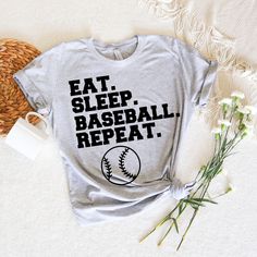 a t - shirt that says eat sleep baseball repeat on it next to some flowers