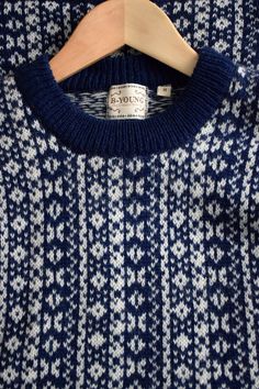 a blue and white sweater is hanging on a wooden hanger with a tag attached to it