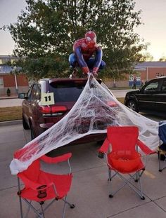 a spider man sitting on top of a car with two red chairs in front of it