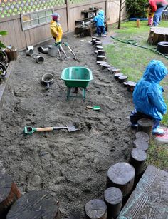 two children in raincoats are playing in the sand with shovels and wheelbarrows