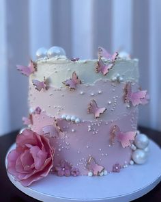 a pink cake with white frosting and butterflies on it, next to a flower