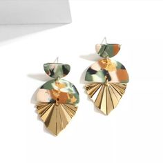 a pair of gold and green earrings on top of a white surface with an object in the background