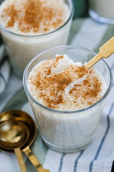 two glasses filled with pudding on top of a blue and white towel next to gold spoons