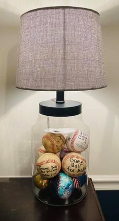 a glass jar filled with baseballs under a lampshade on top of a wooden table