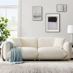 a living room with white couches and pictures on the wall above them, along with potted plants