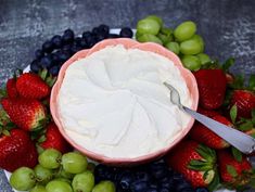 a bowl of whipped cream surrounded by grapes, strawberries and green apples on a plate