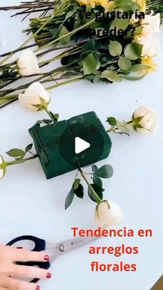 a person cutting flowers with scissors on a white table and the words tendencia en arregls florales written in spanish