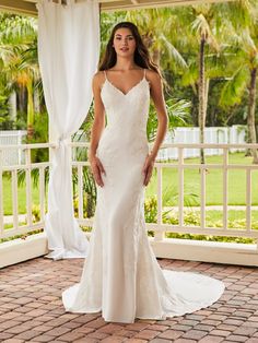 a woman in a white wedding dress standing on a brick patio with palm trees behind her