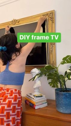 a woman holding up a sign that says diy frame tv in front of her