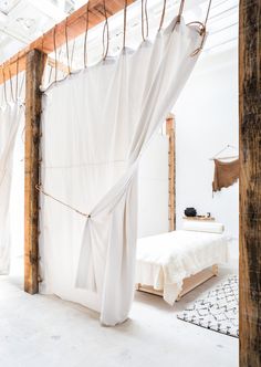 a bed with white curtains hanging from the ceiling