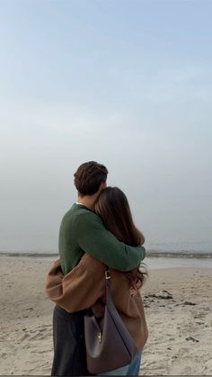 a man and woman hug on the beach while looking out at the ocean from behind them