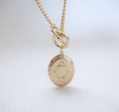 Oval Locket Toggle Necklace Details : - Oval locket to keep secret messages/photographs of your loved ones close to your heart - suspended on curb chain, finished with toggle clasp - made of 16K gold plated over brass - necklace length : 18 inches - pendant : 32 mm x 21 mm - photo compartment : 20 mm x 15 mm Vintage Charm Oval Link Necklace As Gift, Oval Link Necklaces With Vintage Charm For Gifts, Gold-tone Locket Chain Necklace As Gift, Gold-tone Chain Necklace With Locket For Gift, Oval Pendant Locket Necklace With Adjustable Chain For Keepsake, Gold Oval Link Toggle Necklace Gift, Gold Oval Link Toggle Necklace As Gift, Gold Toggle Necklace With Oval Links As Gift, Oval Link Engraved Chain Necklace As Gift