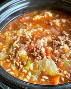 a crock pot filled with meat and cabbage soup on top of a wooden table