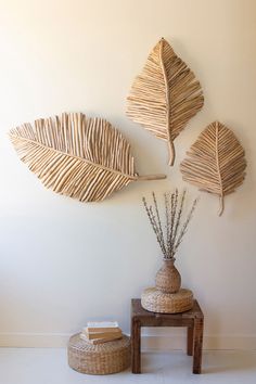 three wicker leaves hang on the wall next to a small table with two vases