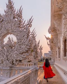 a woman in a red dress is walking down a white building with intricate carvings on it