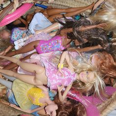 many barbie dolls are laying on the floor in a wicker basket, one is wearing a pink dress