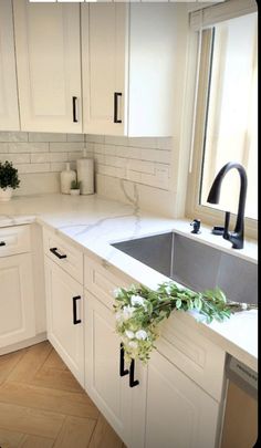 a kitchen with white cabinets and black handles on the counter top, has a sink in it