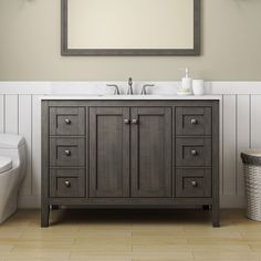 a white toilet sitting next to a bathroom sink under a mirror on top of a wooden cabinet