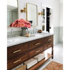 a bathroom with two sinks, mirrors and flowers on the counter top in front of it