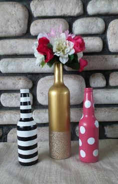 three vases with flowers in them sitting on a table next to a brick wall