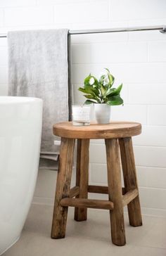 a small wooden stool next to a bath tub with a potted plant on it