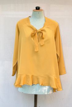 The  blouse is made of mustard yellow polyester crepe fabric. The shape blouses is wide and asymmetric (shorter in the front) and has a large ruffle on the blouse edge. You can tie the neckline or leave it open. Blouse length: Back: 70cm - Front: 50 cm Size: Fr  One size fit (38 to 42) Composition: 100% Polyester Care of clothing: Wash 30oC - Cool iron - Dry cleaning https://www.etsy.com/fr/shop/VLbasics?ref=seller-platform-mcnav Chic Yellow Blouse For Fall, Gold Ruffled Blouse For Spring, Chic Gold Blouse With Ruffles, Chic Mustard Blouse For Fall, Yellow Ruffled Long Sleeve Blouse, Chic Tie Neck Flowy Blouse, Yellow Long Sleeve Blouse With Ruffles, Chic Yellow Blouse, Yellow V-neck Ruffle Blouse