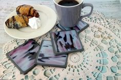 a cup of coffee and four coasters on a doily next to a plate with pastries